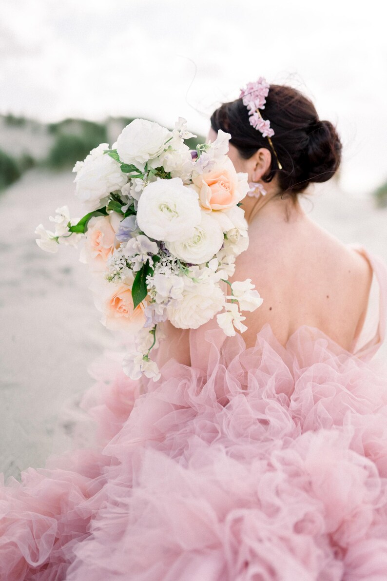 May include: A bride wearing a pink tulle dress with a large bouquet of white and peach flowers. The bouquet is held in front of her, obscuring her face.