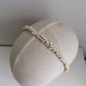 May include: A white pearl headband with a gold wire base. The headband is on a white fabric covered mannequin head.