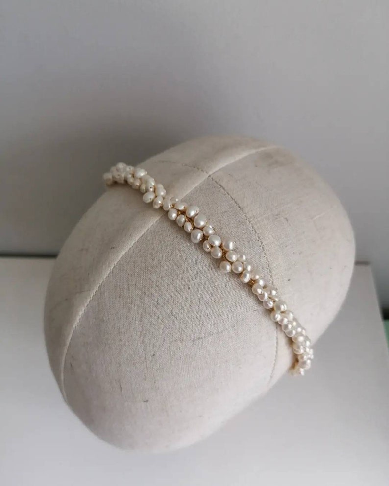 May include: A white pearl headband with a gold wire base. The headband is on a white fabric covered mannequin head.