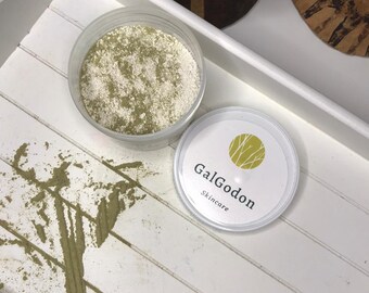 May include: A white container with a green powder inside, labeled "GalGodon Skincare". The powder is spilled on a white wooden surface.