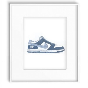 May include: A blue and white Nike Dunk Low sneaker with a white swoosh logo. The sneaker is framed in a white frame.