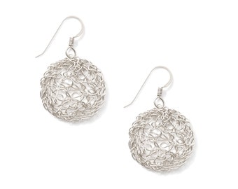 May include: A pair of silver-colored earrings. Each earring features a spherical design crafted from interwoven wire, suspended from a simple hook. The earrings are displayed against a white background, highlighting their intricate, openwork texture.