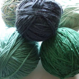 May include: Five balls of yarn in various shades of green and blue. The yarn is arranged in a circle on a white surface.