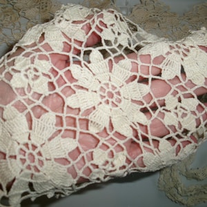 May include: Close-up of a delicate, off-white crocheted lace fabric with a floral pattern. The lace is soft and intricate, with a delicate texture.