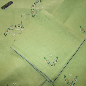 May include: Set of four green linen napkins with embroidered white daisies. The napkins have a gray trim and are folded in a square shape.