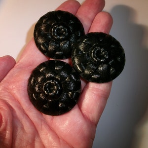 May include: Three black buttons with a raised, circular, woven design. The buttons are in a hand.