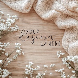 May include: A flat lay image of a wooden surface with white baby's breath flowers and a beige knitted blanket. The text "YOUR DESIGN HERE" is written in black on the wood.