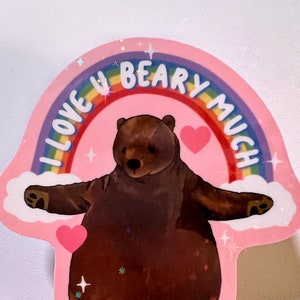 May include: A pink sticker with a rainbow arch that says "I love you beary much". A brown bear with pink hearts is standing in the middle of the rainbow arch.