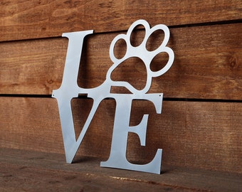 May include: Metal wall decor featuring the word "LOVE" with a paw print replacing the "O". The letters are silver and the paw print is cut out.