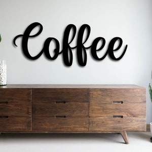 Può includere: Un cartello in legno nero con la parola "Coffee" scritta in corsivo. Il cartello è appeso a un muro bianco sopra una cassettiera in legno con sei cassetti.