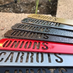 K&ouml;nnte beinhalten: Ein Satz von sechs Gartenmarkierungen aus Metall mit verschiedenen Farbt&ouml;nen. Die Markierungen sind mit "ONIONS", "CARROTS", "ONIONS", "ONIONS", "SPINACH" und "ONIONS" beschriftet.