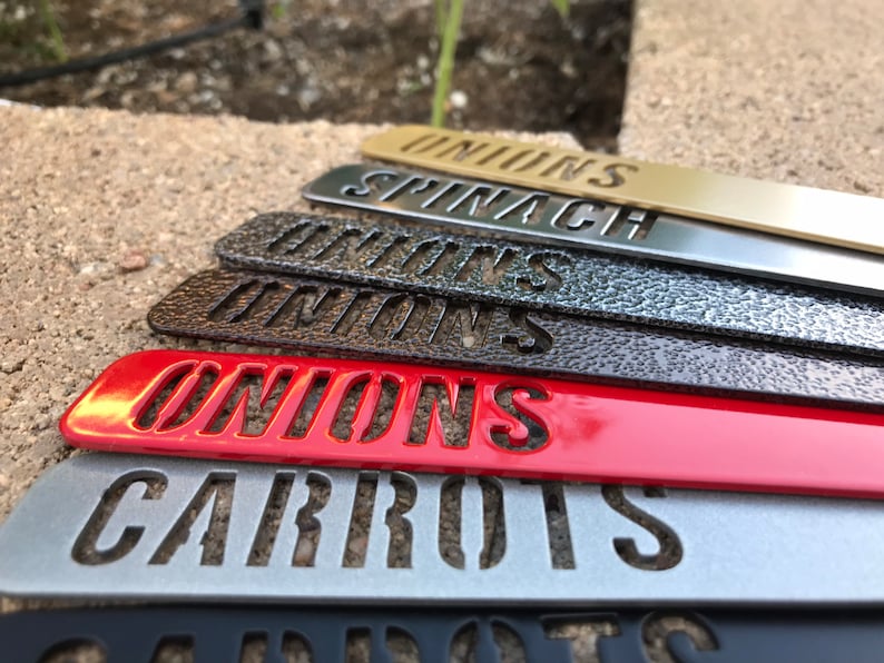 K&ouml;nnte beinhalten: Ein Satz von sechs Gartenmarkierungen aus Metall mit verschiedenen Farbt&ouml;nen. Die Markierungen sind mit "ONIONS", "CARROTS", "ONIONS", "ONIONS", "SPINACH" und "ONIONS" beschriftet.