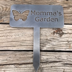 Puede incluir: Una estaca de jard&iacute;n de metal con un recorte de mariposa y el texto "Momma's Garden".