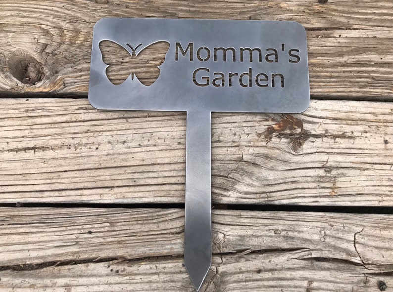 Puede incluir: Una estaca de jard&iacute;n de metal con un recorte de mariposa y el texto "Momma's Garden".