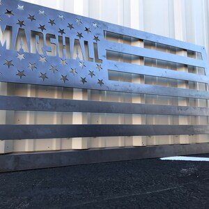 May include: A metal American flag with the word "MARSHALL" cut out of the stars. The flag is made of a dark metal and has a rustic look.