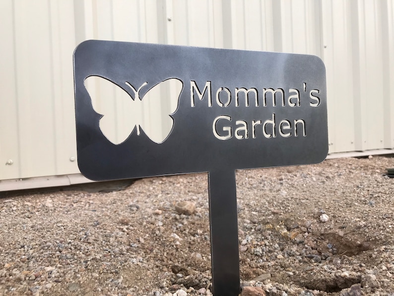 Puede incluir: Un letrero de jard&iacute;n de metal negro con un recorte de mariposa y el texto "Momma's Garden".