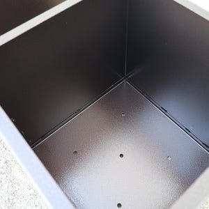 May include: A brown metal planter with a square shape and a textured finish. The planter has several drainage holes in the bottom.