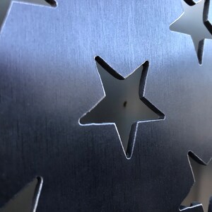 May include: A close-up of a metal sheet with a pattern of cut-out stars. The metal has a brushed finish, giving it a textured look.