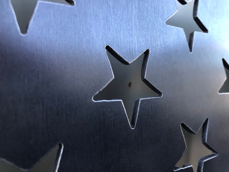 May include: A close-up of a metal sheet with a pattern of cut-out stars. The metal has a brushed finish, giving it a textured look.