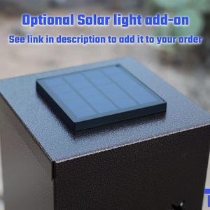 May include: A dark brown metal box with a solar panel on top. The solar panel is black and has a grid pattern. The text "Optional Solar light add-on" is in blue above the box.