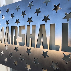 May include: A metal sign with a star pattern background and the word "MARSHALL" cut out in the center.