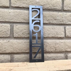 May include: A metal house number sign with the numbers 2617 cut out. The sign is black and has a modern design.