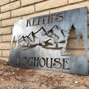Peut inclure: Une plaque en métal avec le texte "Keith's Doghouse" et une silhouette de montagnes et d'arbres. La plaque est patinée et a un aspect rustique.