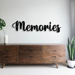 May include: A dark brown wooden dresser with six drawers and a black metal sign that reads "Memories" on a white wall.