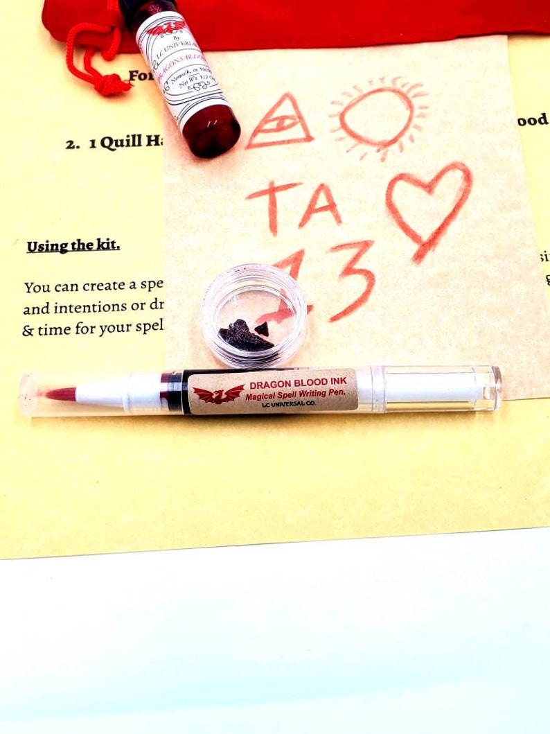 May include: A close-up of a kit for creating spells. The kit includes a quill, a bottle of red ink, a small jar of black powder, and a pen labeled "Dragon Blood Ink Magical Spell Writing Pen." The kit also includes a piece of paper with a triangle, a sun, a heart, and the letters "TA" and the number "13" drawn on it. The text "Using the kit. You can create a spell and intentions or draw & time for your spell" is written on the paper. The text "2. 1 Quill H:" is written on the paper.