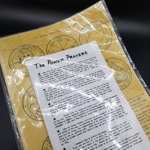 May include: A set of seven yellow paper pentacles with black ink designs. The pentacles are surrounded by a plastic bag. The text "The Power Prayers" is printed on a white paper with black text.