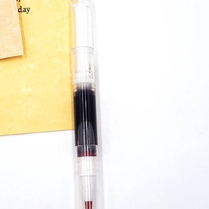 May include: A clear plastic tube with a black and red liquid inside. The tube has a white cap and a red tip.