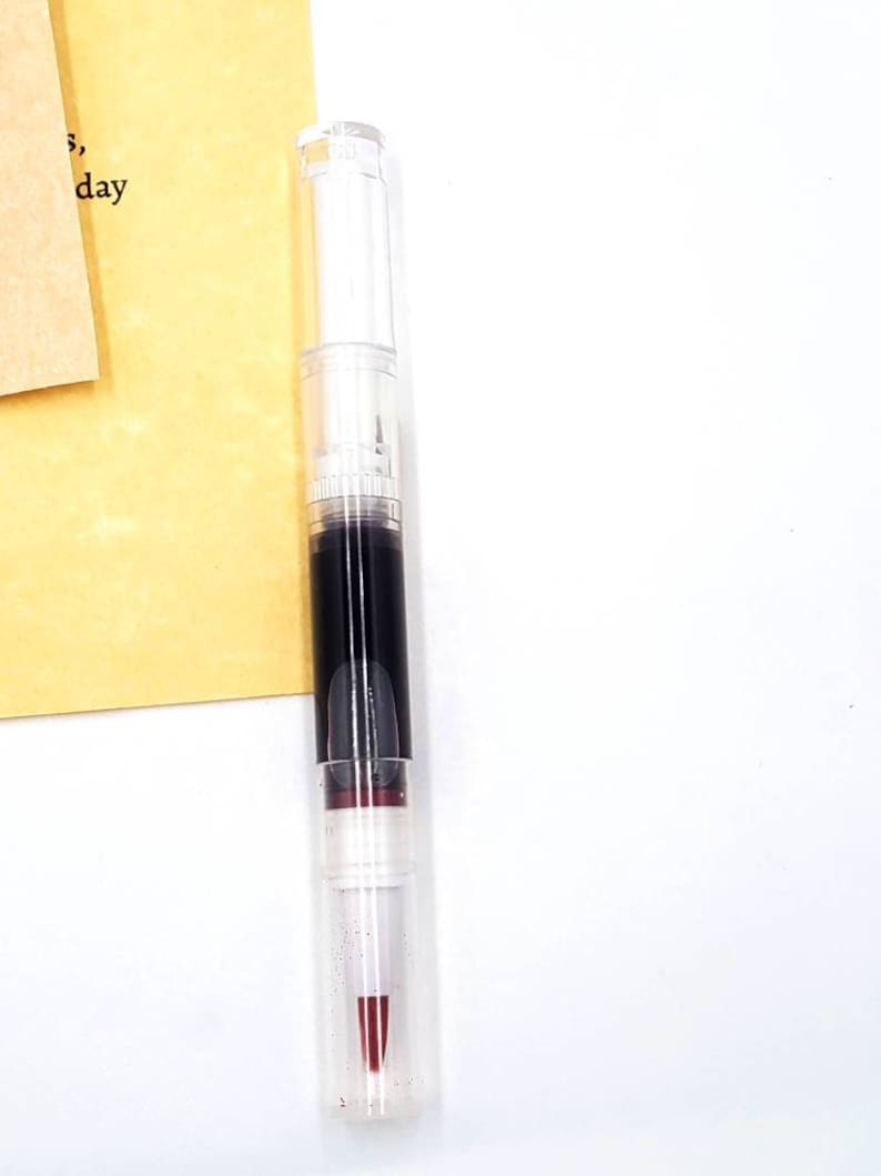 May include: A clear plastic tube with a black and red liquid inside. The tube has a white cap and a red tip.