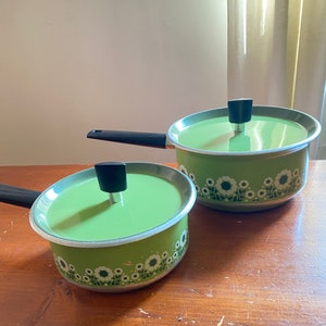 Peut inclure: Deux casseroles vertes avec des motifs floraux blancs et des poignées noires. La plus petite casserole est au premier plan et la plus grande est à l'arrière-plan.