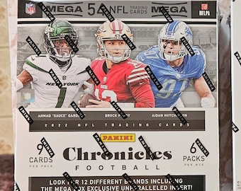 May include: A box of 2022 Panini Chronicles Football trading cards. The box is white with black and red accents. The front of the box features three football players: one in a green and white uniform, one in a red and gold uniform, and one in a blue and white uniform. The box also features the Panini logo and the text "2022 Panini Chronicles Football".
