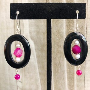 May include: Black oval earrings with a pink and white agate stone and a pink agate dangle. The earrings are silver.