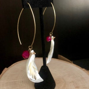 May include: A pair of gold hoop earrings with a white shell and a red gemstone dangling from each hoop.