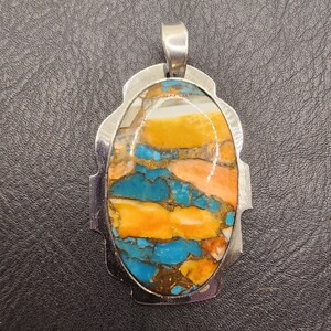 May include: A silver pendant featuring a large oval turquoise stone. The stone is a mix of blue, orange, and white colours.