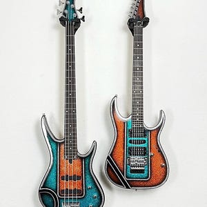 May include: Two electric guitars hanging on a white wall. One is a bass guitar with a teal and orange finish. The other is a six-string guitar with a similar color scheme. Both have black hardware and are mounted on black wall hangers.