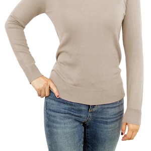 May include: A light brown long-sleeved sweater with a v-neck and a ribbed hem. The sweater is worn over a pair of blue jeans.