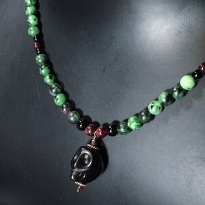 May include: A green, black and red gemstone beaded necklace with a black skull pendant.