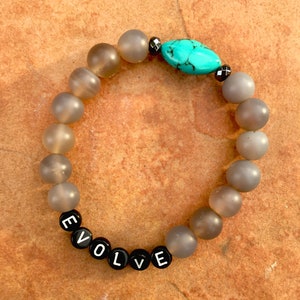 May include: Grey beaded bracelet with a turquoise stone and black beads spelling out the word "EVOLVE".