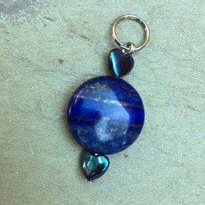 May include: A blue lapis lazuli stone pendant with a silver ring at the top and two iridescent blue heart-shaped beads.