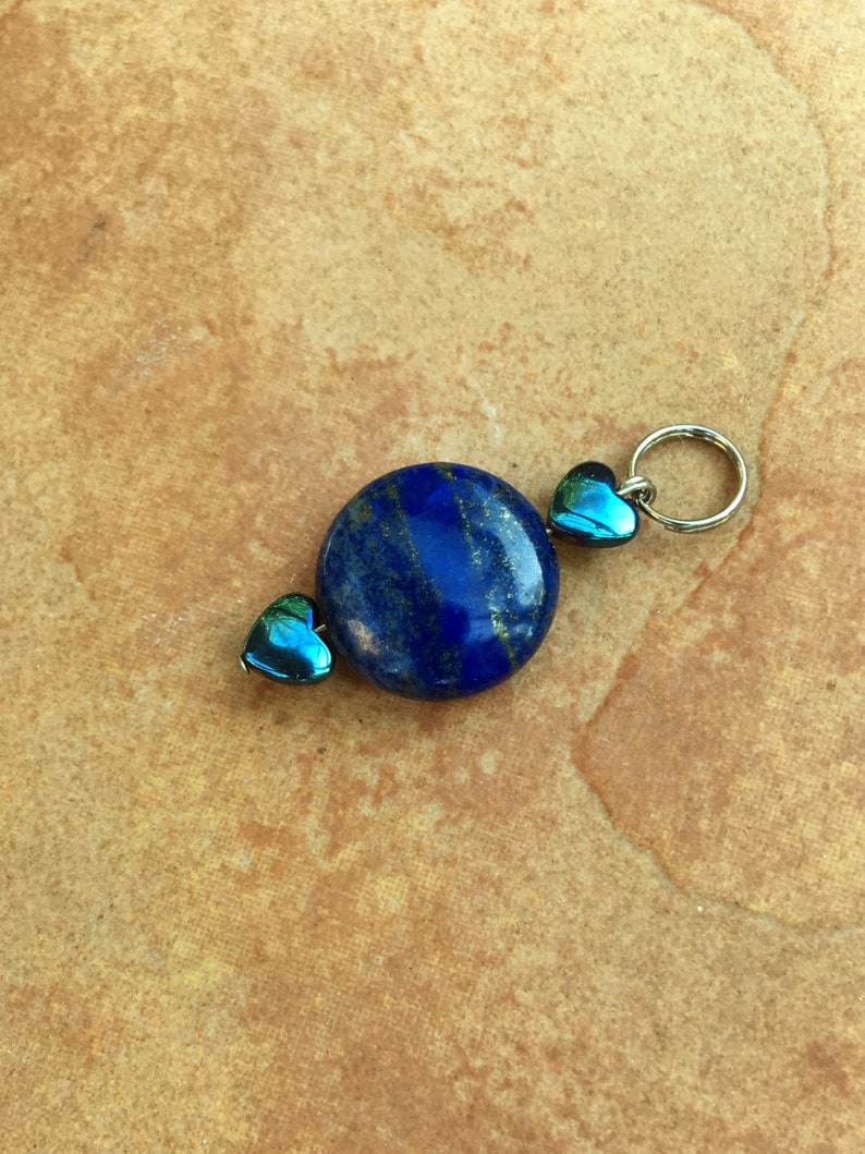 May include: A blue lapis lazuli gemstone pendant with two iridescent blue heart-shaped beads on a silver chain.