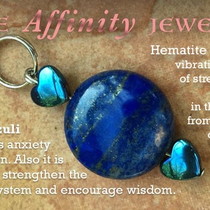 May include: A blue Lapis Lazuli stone pendant with silver accents and two teal heart-shaped charms. The pendant is on a brown background with text that reads "Lapis Lazuli discharges anxiety and tension. Also it is thought to strengthen the immune system and encourage wisdom." Hematite has calming vibrations in times of stress or worry. It also aids in the recovery from any illness of the blood.