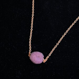 May include: A delicate rose gold chain necklace with a single, round, purple gemstone pendant.