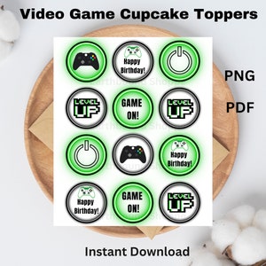 May include: Printable cupcake toppers featuring a green and black video game theme. The toppers include images of a game controller, a power button, and the words "Level Up" and "Game On!"