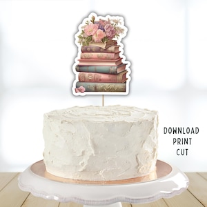 Puede incluir: Una tarta blanca glaseada con una decoración. La decoración presenta una pila de libros antiguos coronada con flores rosas y moradas. El texto "DOWNLOAD PRINT CUT" es visible en el lado derecho de la tarta.