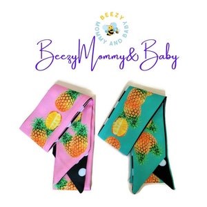 May include: Two reversible hair scrunchies with a pineapple print on one side and black and white polka dots on the other. One scrunchie is pink and the other is teal.