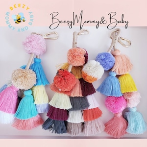 May include: Three colorful tassel keychains with pom poms. Each keychain has a different color scheme and features multiple layers of tassels. The keychains are labeled "Beezy Mommy & Baby".