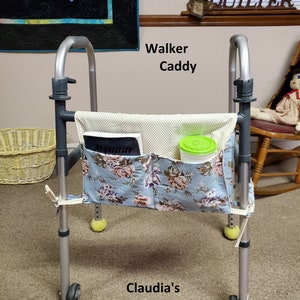 May include: A walker caddy with a floral print pocket and a cream-colored polka dot pocket. The caddy is attached to a silver walker. The text "Walker Caddy" and "Claudia's QuiltShoppe" are visible.